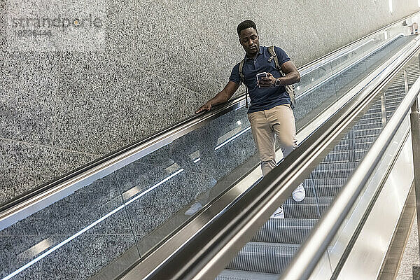 Mann benutzt Mobiltelefon und bewegt sich auf Rolltreppe nach unten
