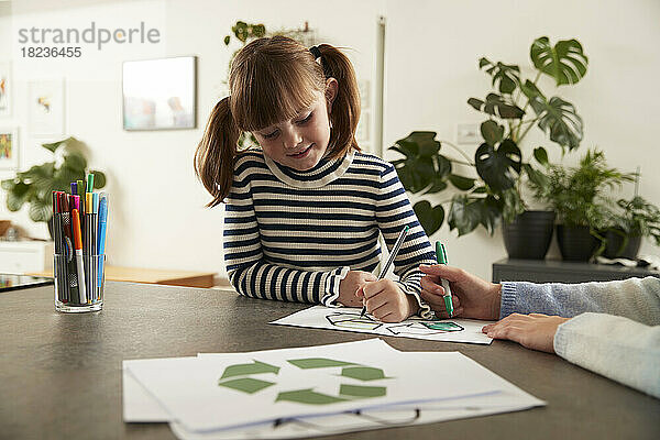Lächelndes süßes Mädchen mit Schwester  das zu Hause Recycling-Symbol mit Stift ausmalt