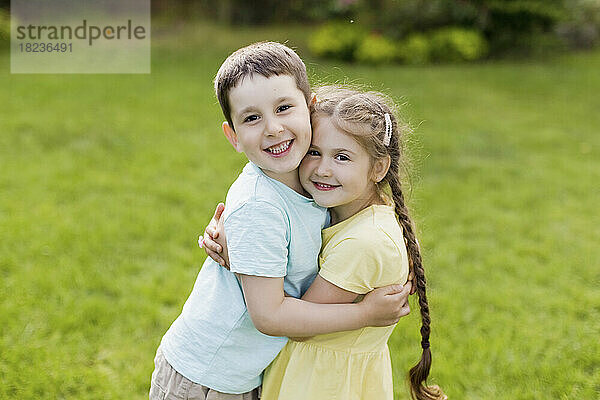 Lächelnder Bruder umarmt Schwester  die im Garten steht