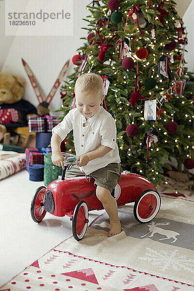 Junge spielt mit Spielzeugauto neben dem Weihnachtsbaum zu Hause