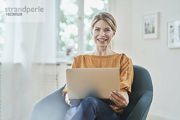 Glückliche Geschäftsfrau mit Laptop im Sessel sitzend