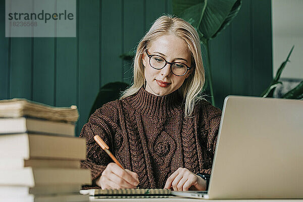 Geschäftsfrau mit Brille schreibt im Heimbüro Tagebuch