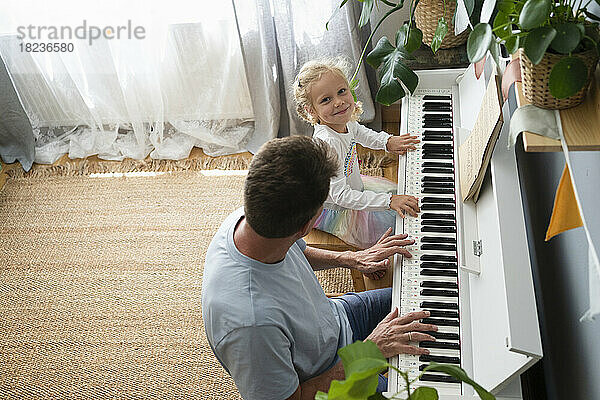 Man teaching piano to daughter at home