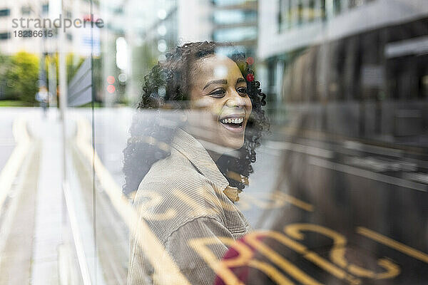 Happy woman talking to friend at bus stop seen through glass