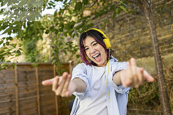 Fröhliche Frau mit kabellosen Kopfhörern gestikuliert im Garten