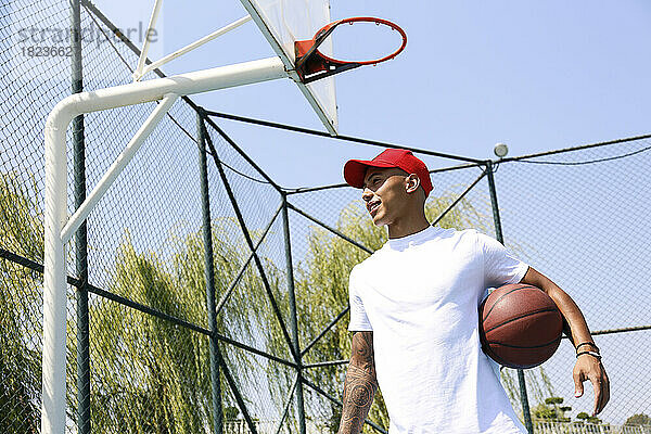 Junger Mann hält an sonnigem Tag Basketball unter dem Arm