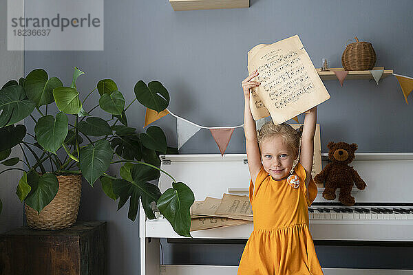 Nettes Mädchen hält Notenblätter am Klavier zu Hause