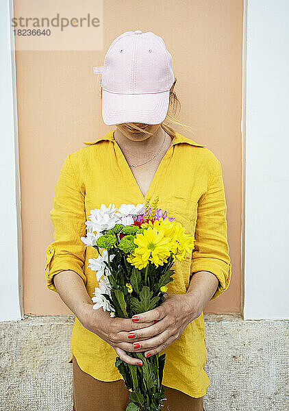 Junge Frau mit Mütze steht mit Blumen vor der Wand