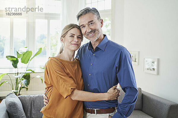 Lächelndes Paar umarmt sich zu Hause vor dem Sofa