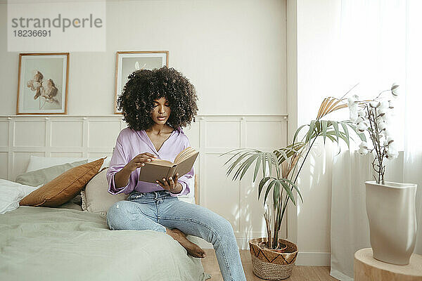 Afro-Frau liest ein Buch und sitzt auf dem Bett im Schlafzimmer