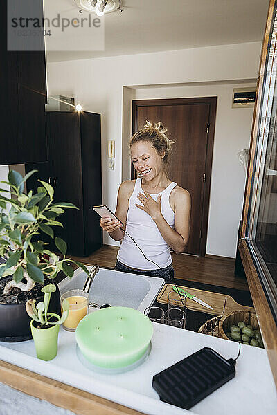 Glückliche Frau  die in der Küche auf ihr Mobiltelefon schaut
