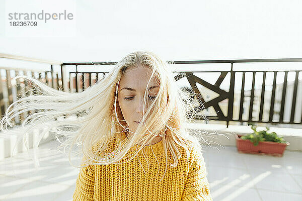 Blonde Frau mit windgepeitschten Haaren auf der Terrasse