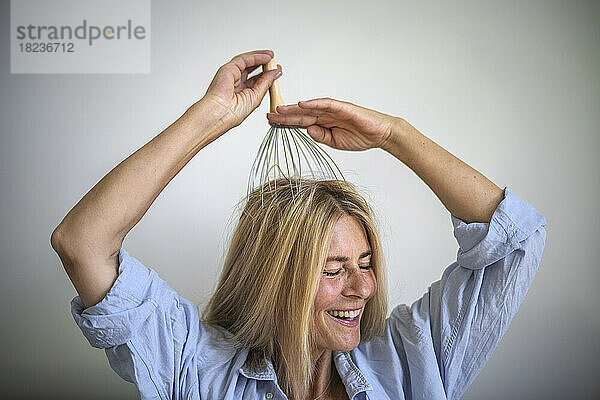 Glückliche Frau genießt zu Hause eine Kopfhautmassage mit einem Massagegerät