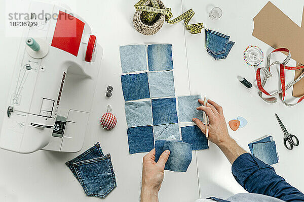 Hände eines Modedesigners  der auf dem Tisch an Jeansstücken arbeitet