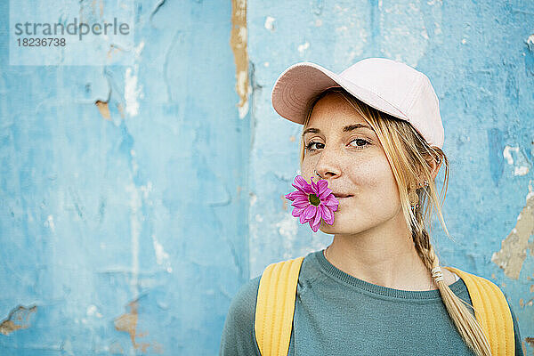 Junge Frau mit Mütze und rosa Blume im Mund