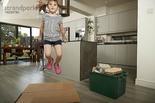 Mädchen springt zu Hause über gefalteten Karton