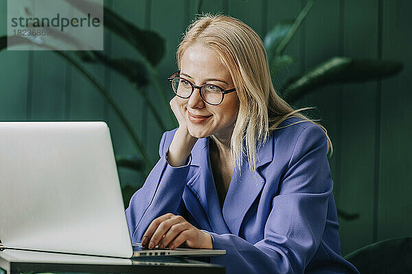 Lächelnde Geschäftsfrau benutzt Laptop im Heimbüro