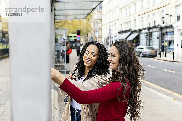 Fröhliche Freunde berühren die Wand auf dem Fußweg an der Bushaltestelle