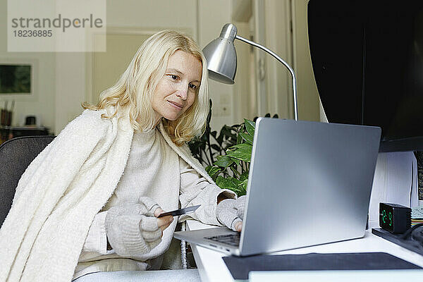 Frau mit Kreditkarte sitzt zu Hause vor Laptop
