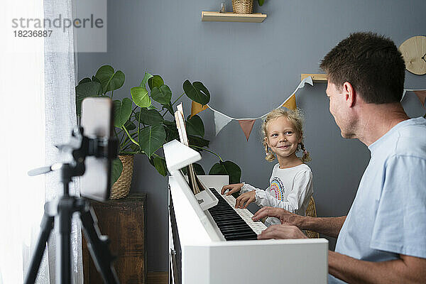 Lächelndes Mädchen  das zu Hause mit seinem Vater Klavier spielt