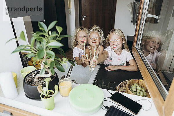 Glückliche Mädchen zeigen hölzerne Zahnbürsten in der Küche