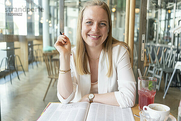 Glückliche Geschäftsfrau mit Zeitschrift sitzt am Tisch im Café