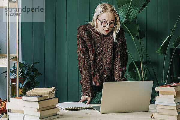 Geschäftsfrau trägt Pullover und schaut im Heimbüro auf den Laptop