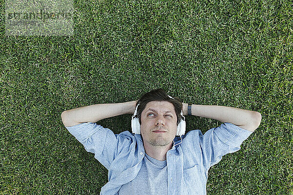 Mann trägt Kopfhörer und entspannt sich im Gras im Park
