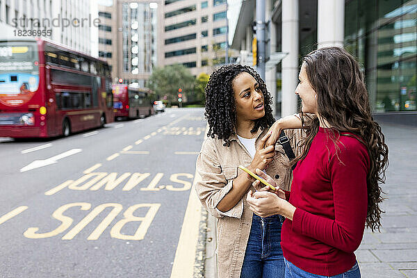 Frau unterhält sich mit Freundin an Bushaltestelle