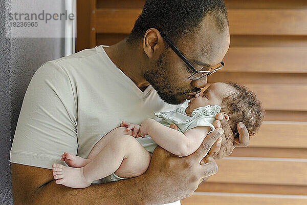 Vater küsst süßes kleines Mädchen vor Holzwand