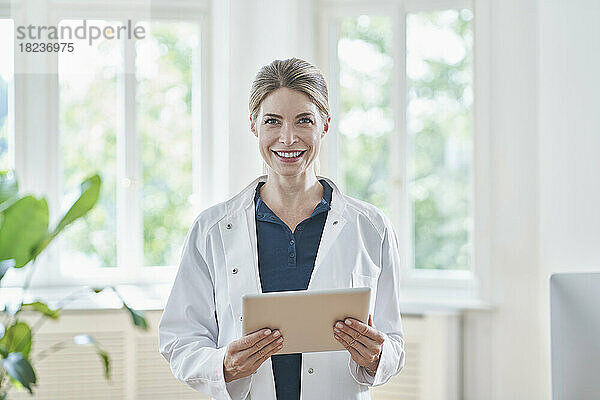 Glückliche Ärztin steht mit Tablet-PC in der Arztpraxis