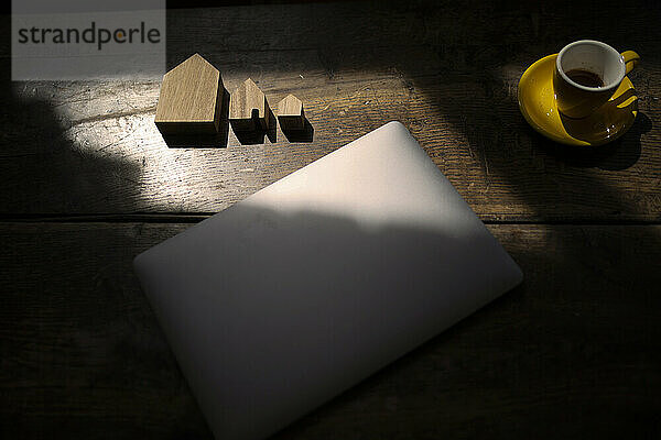 Model house and laptop by cup on table