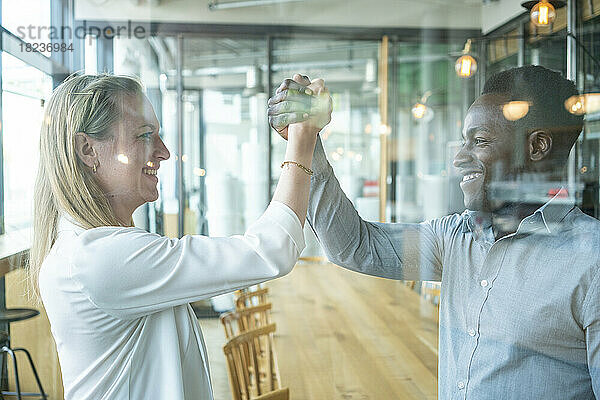 Glücklicher Geschäftsmann und Geschäftsfrau halten Händchen und feiern den Erfolg im Café