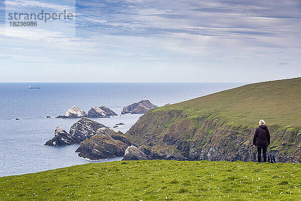 UK  Scotland  Unst  Female hiker standing on clifftop looking toward Muckle Flugga Lighthouse