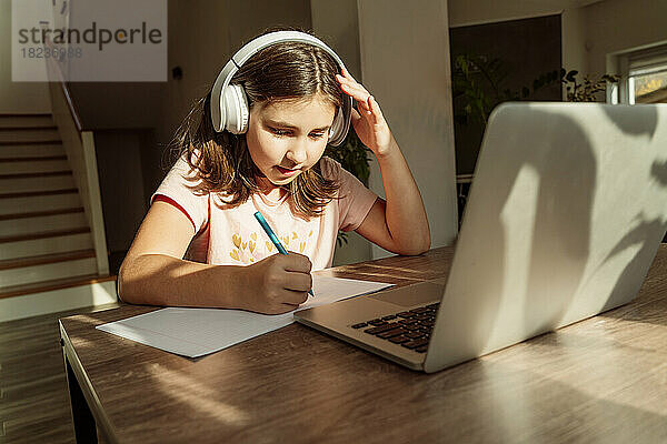Mädchen mit kabellosen Kopfhörern lernt zu Hause