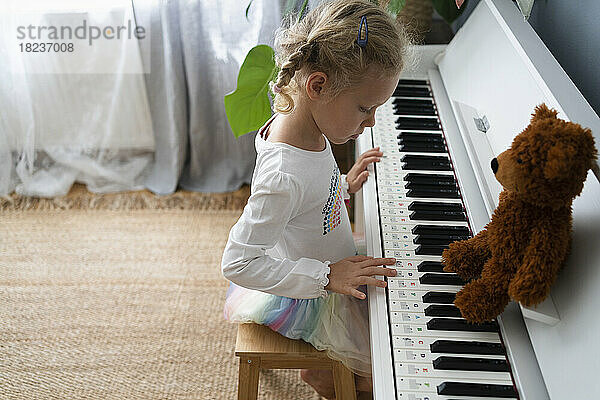 Mädchen lernt zu Hause mit Teddybär Klavier spielen