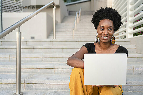Glückliche Geschäftsfrau mit Laptop sitzt auf Stufen