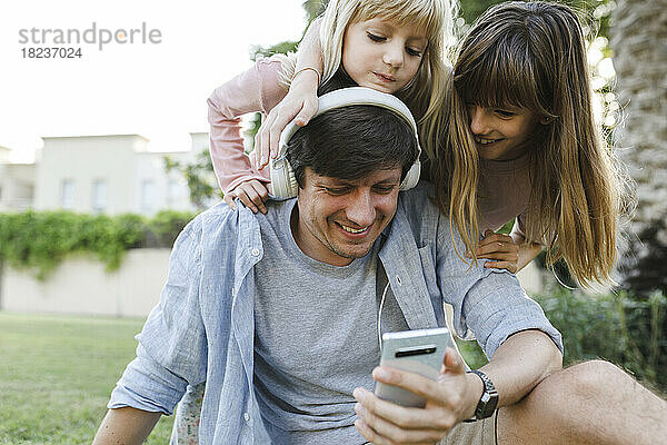 Glücklicher Vater nutzt Smartphone mit Töchtern im Park
