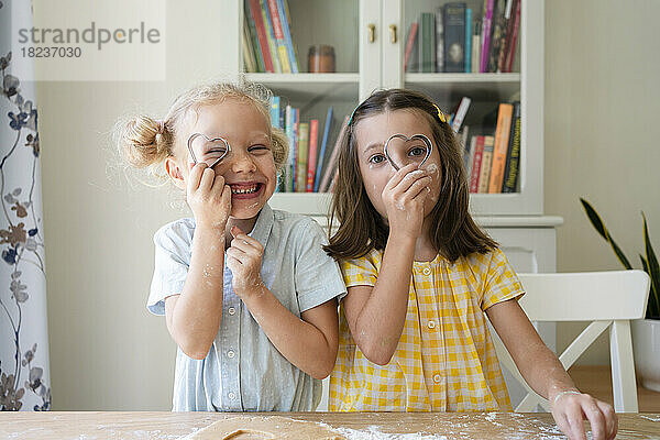 Mädchen schauen zu Hause durch einen herzförmigen Keksausstecher
