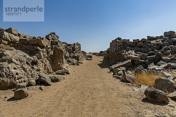 Leere unbefestigte Straße inmitten von Felsen unter blauem Himmel an der archäologischen Stätte Al-Ukhdud in Najran  Saudi-Arabien