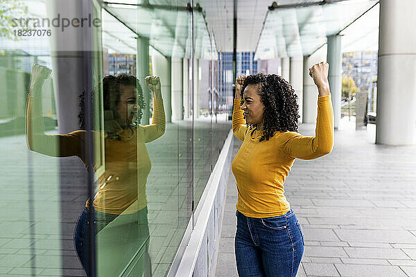 Frau lässt ihre Muskeln spielen und blickt spiegelbildlich auf eine Glaswand