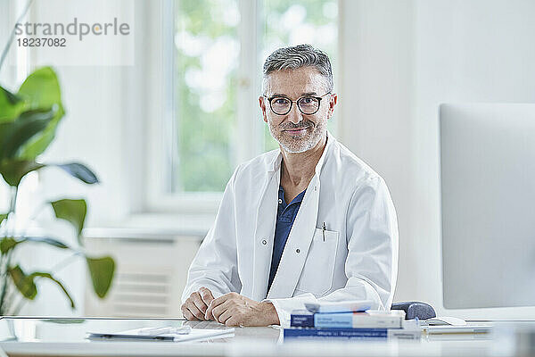 Lächelnder reifer Arzt  der in der Arztpraxis am Schreibtisch sitzt