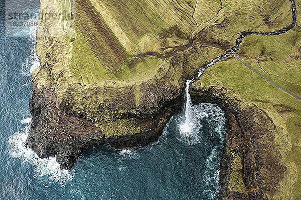 Mulafossur waterfall amidst rocky mountain by sea