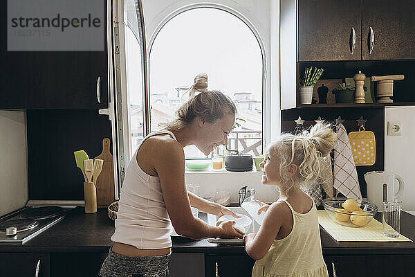 Woman and daughter having fun washing dishes in the kitchen