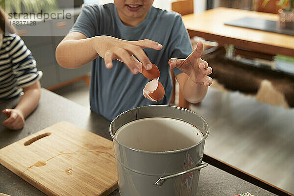 Hand eines Jungen  der zu Hause Eierschale in den Mülleimer wirft