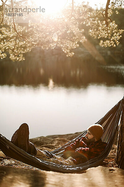 Mann entspannt sich auf Hängematte in der Nähe des Sees an einem sonnigen Tag