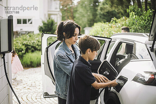 Seitenansicht von Mutter und Sohn beim Aufladen eines Elektroautos vor dem Haus