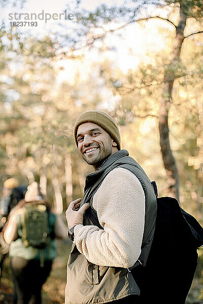 Seitenansicht eines lächelnden Mannes mit Rucksack  der im Wald steht