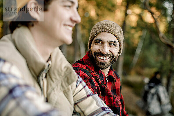 Glücklicher Mann mit kariertem Hemd im Gespräch mit einem männlichen Freund beim Camping