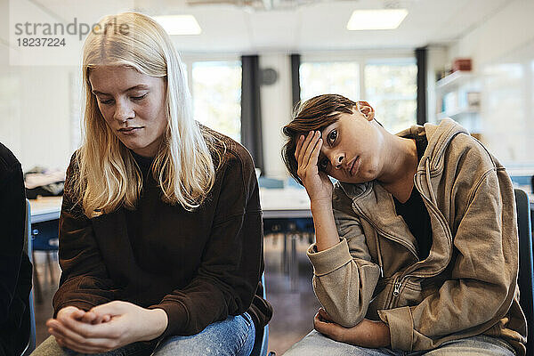 Trauriger Teenager  der während der Therapie bei einem blonden Mädchen im Klassenzimmer sitzt